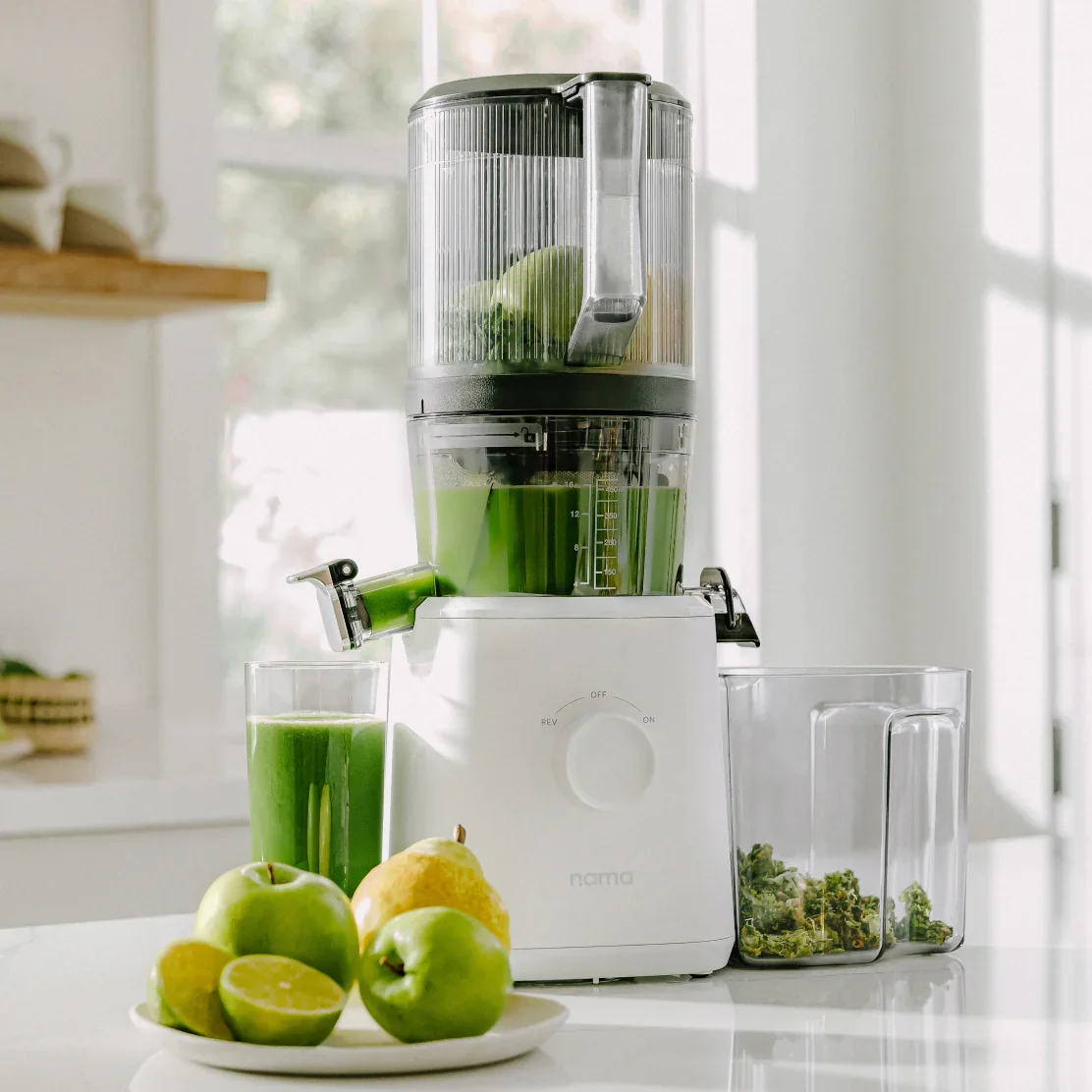 Nama J2 Cold Press Juicer running with green juice flowing into glass, pulp bin alongside