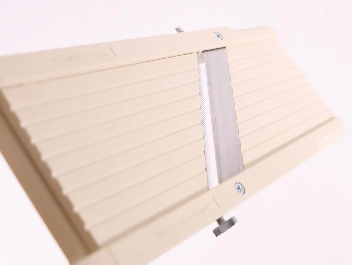 Close-up of the beige Super Benriner No. 95 deck showing the fine-toothed julienne blade fitted in front of the main blade, with the side screws that hold it in place