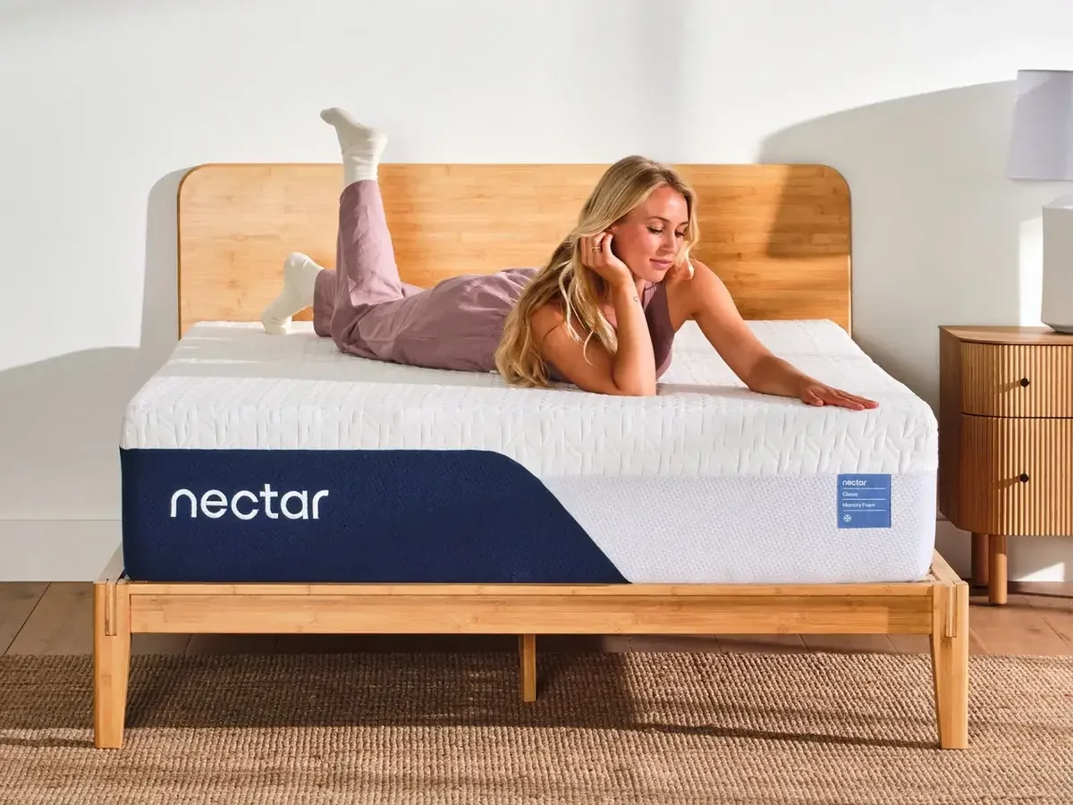 Person lying on Nectar Classic mattress on bamboo bed frame in bright room
