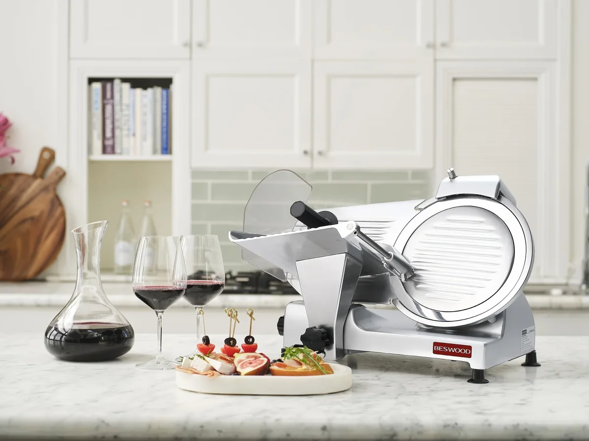 Beswood 10-Inch Electric Deli Meat Slicer on a marble kitchen counter beside wine glasses, a decanter and a charcuterie plate