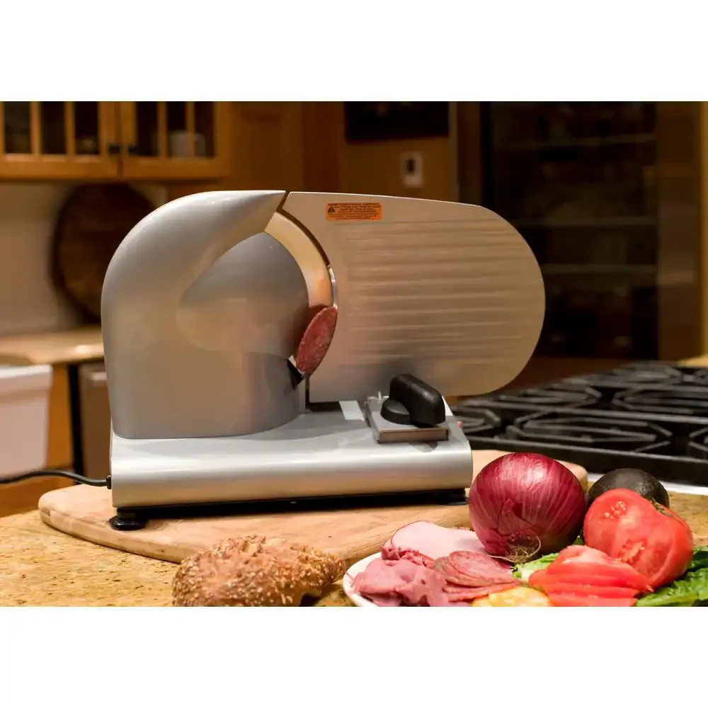Weston 9-Inch Meat Slicer 61-0901-W seen from the rear slicing salami on a kitchen counter, next to a plate of sliced ham, red onion and tomatoes