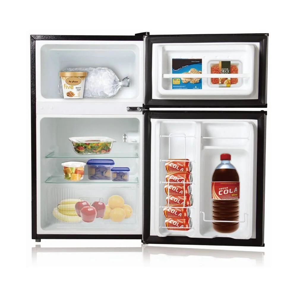Midea WHD-113FB1 double-door mini fridge stocked with groceries, showing ice cream and frozen food in the freezer and produce, drink cans, and a bottle in the fridge and door racks