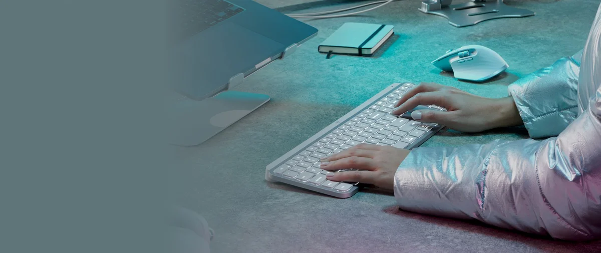 Logitech MX Keys S lifestyle shot with hands typing at a desk alongside laptop and MX Master mouse