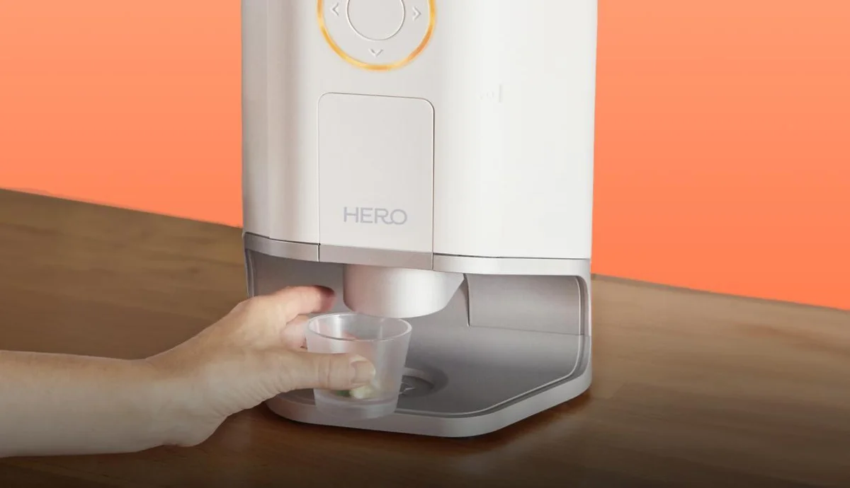 Close-up of the Hero Smart Pill Dispenser dispensing a dose into the included cup being held by hand
