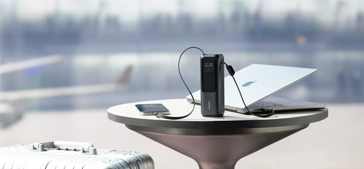Anker Laptop Power Bank 165W on an airport lounge table charging a laptop and a phone through its two built-in cables