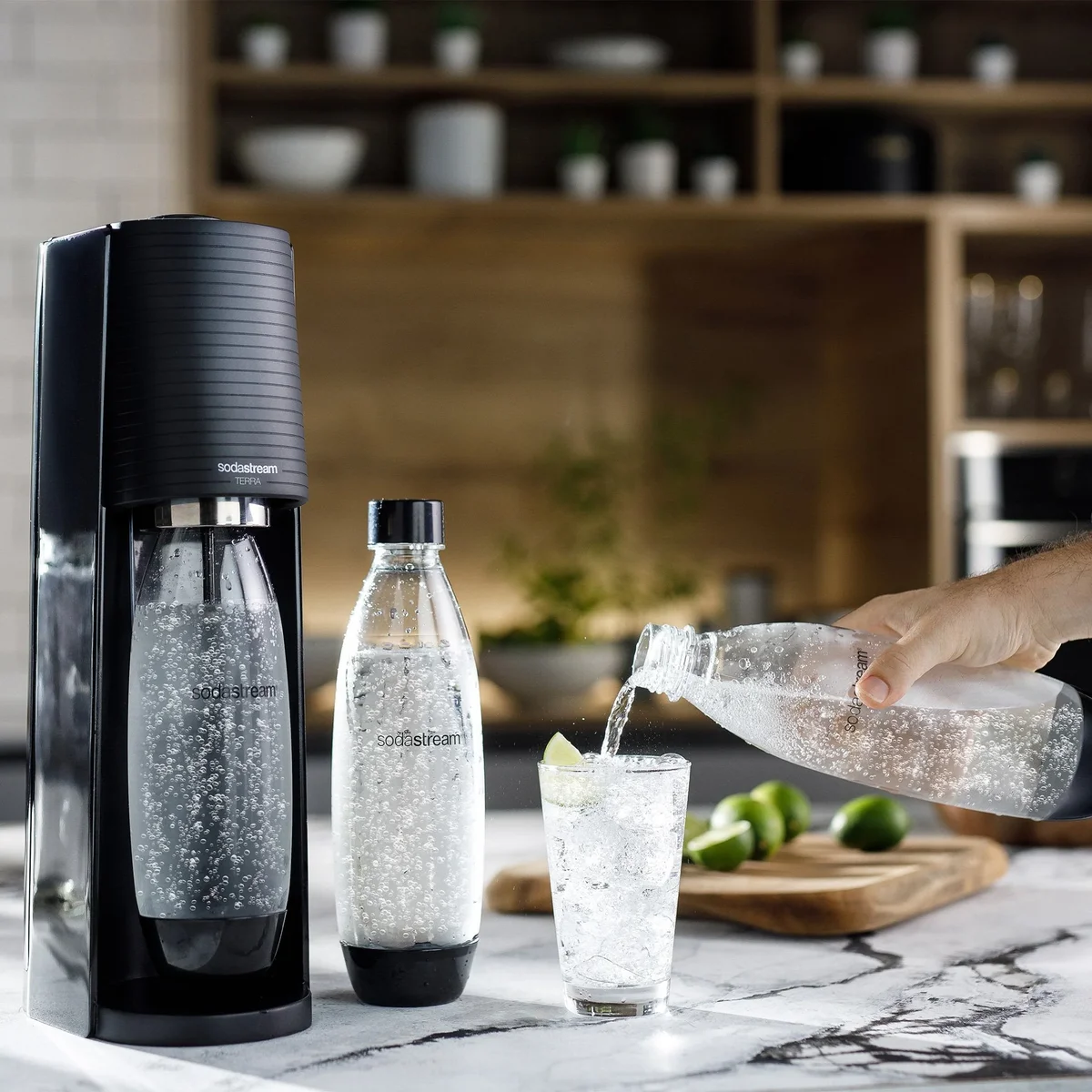 SodaStream Terra in black on a kitchen counter, sparkling water being poured into a glass with lime