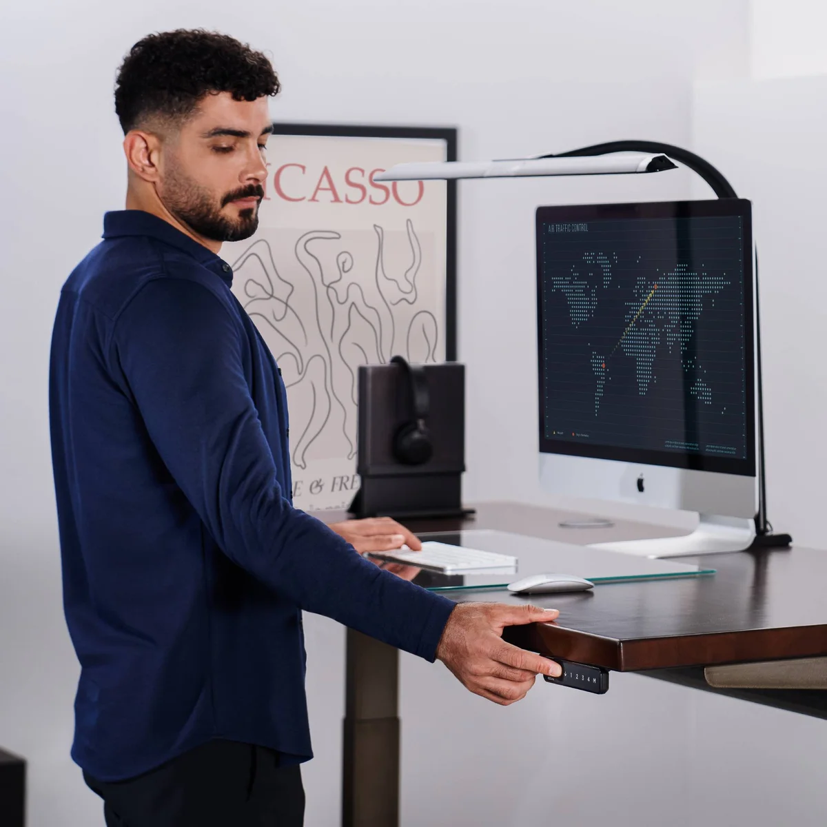 Man standing at a raised UPLIFT V3 Standing Desk with a dark top, pressing the edge-mounted height keypad