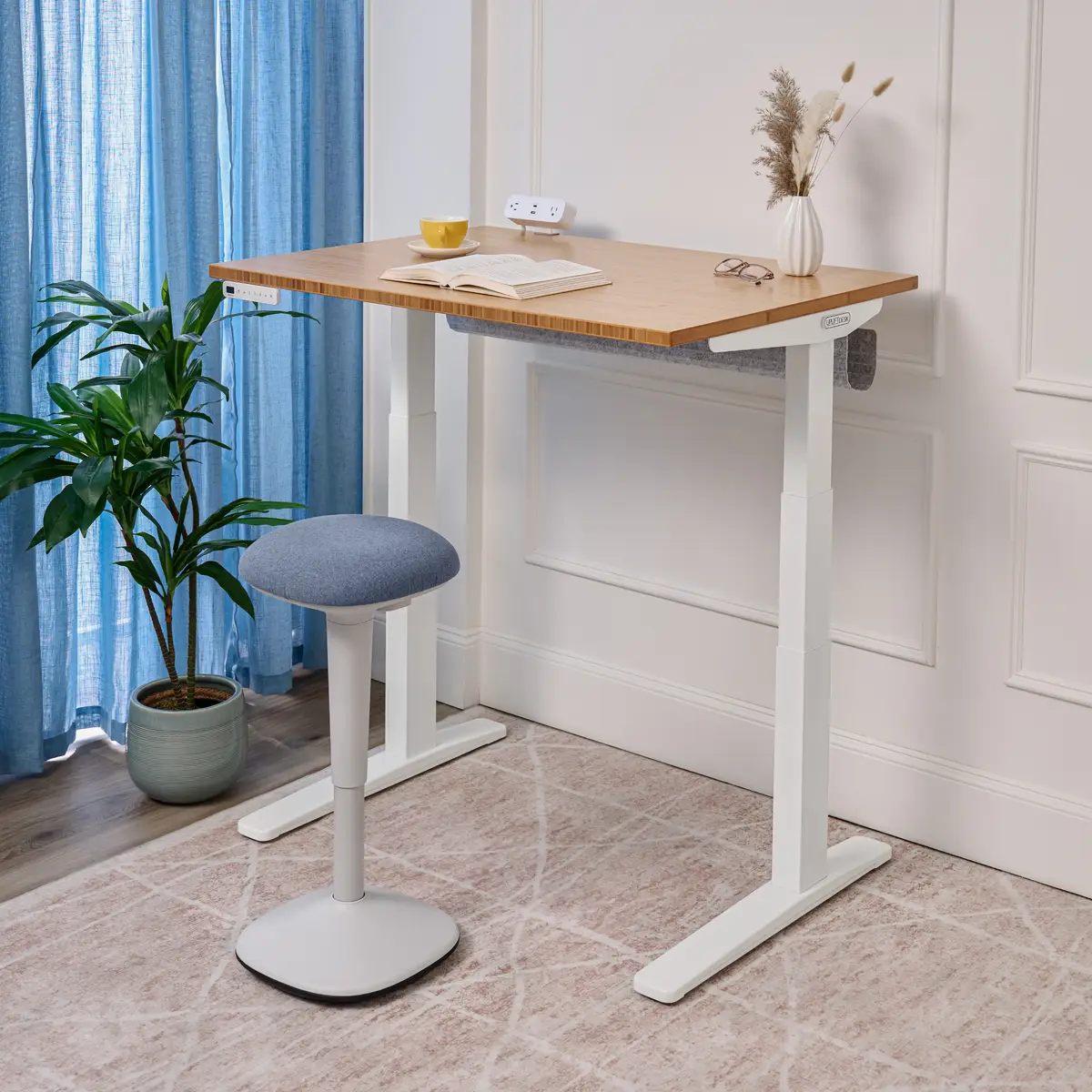 Compact UPLIFT V3 Standing Desk with a bamboo top and white frame raised to standing height beside an active stool