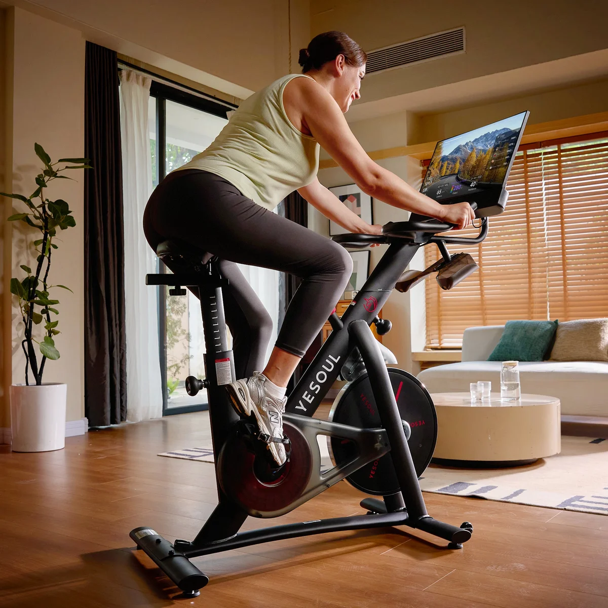 Woman riding the Yesoul G1M Plus in a home living room, watching content on the large screen
