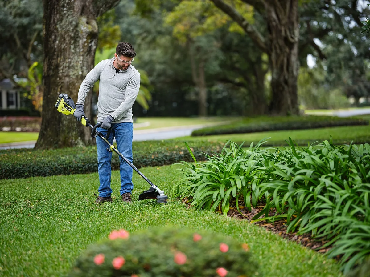 Person using Ryobi 40V string trimmer along garden border