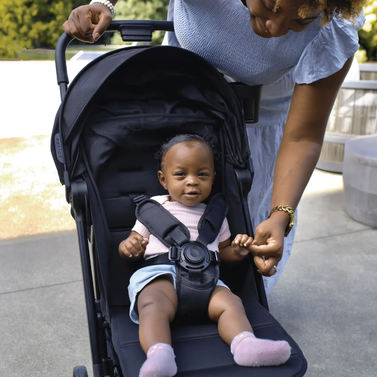 Parent buckling baby into Colugo Compact Stroller+ 5-point harness outdoors
