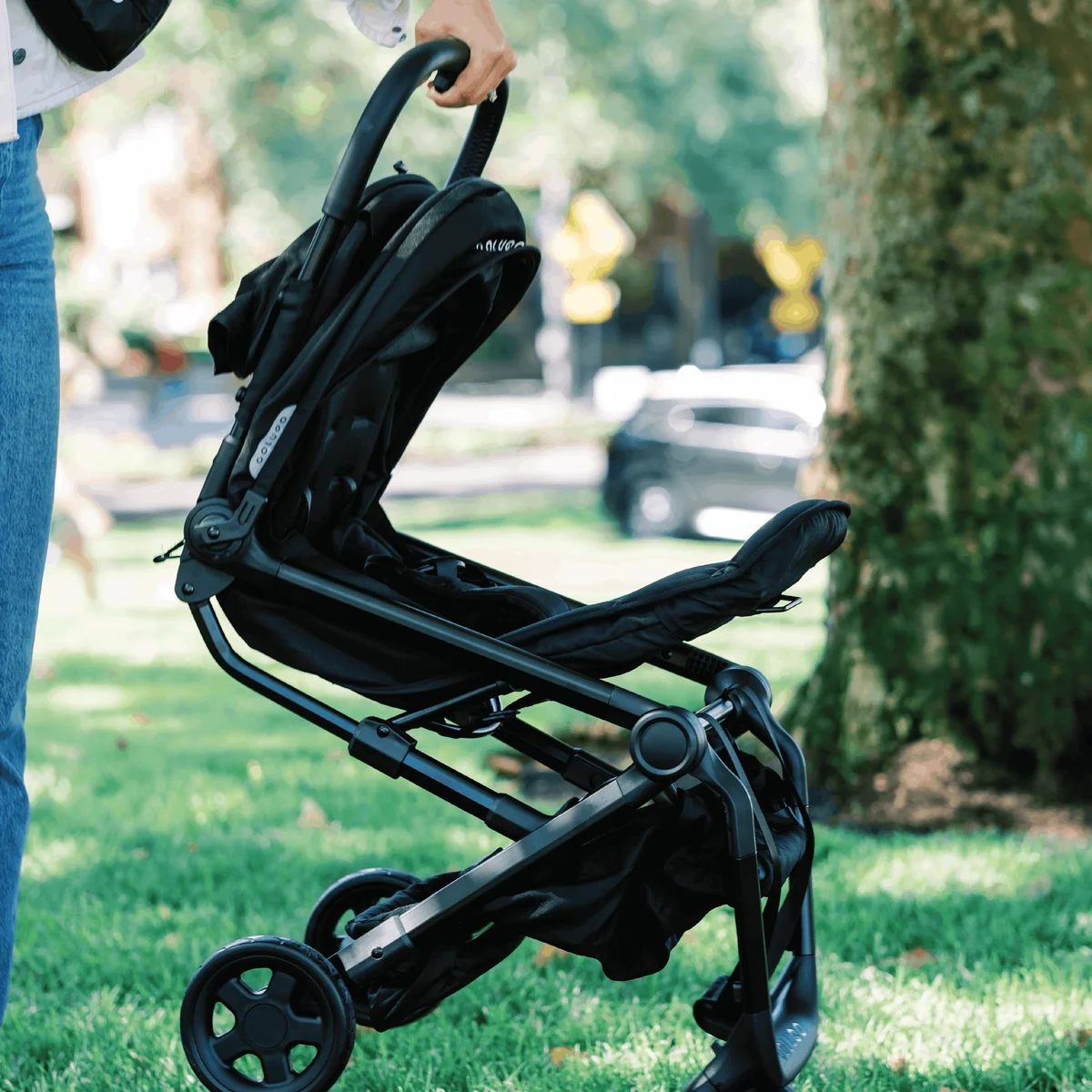 Parent folding Colugo Compact Stroller+ in a park