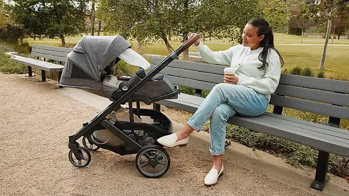 UPPAbaby Cruz V3 in park setting, mother seated on bench with stroller beside her