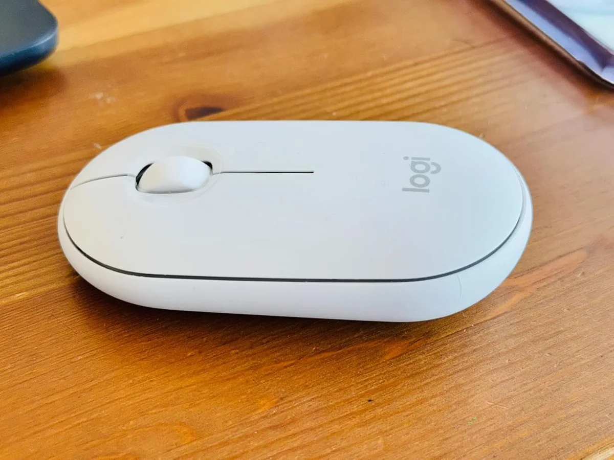 Logitech Pebble Mouse 2 M350s in off-white, overhead real-world view on a wood desk