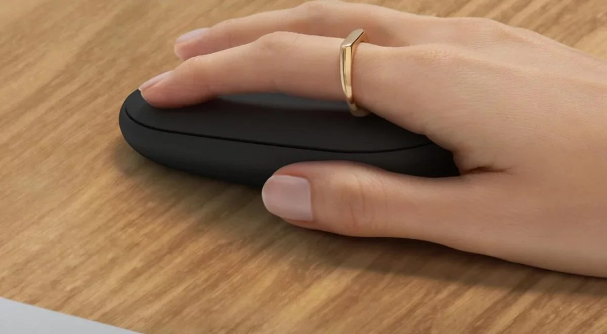 Hand resting on Logitech Pebble Mouse 2 M350s in graphite on a wood desk surface