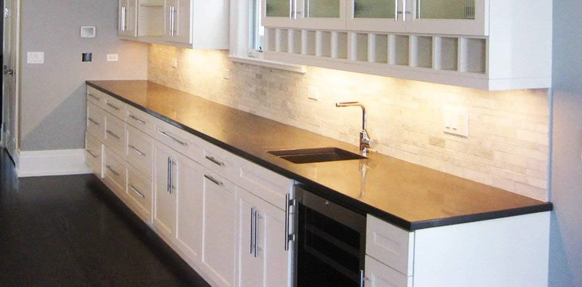 Litever bars lighting a marble tile backsplash above a long counter with white shaker cabinets