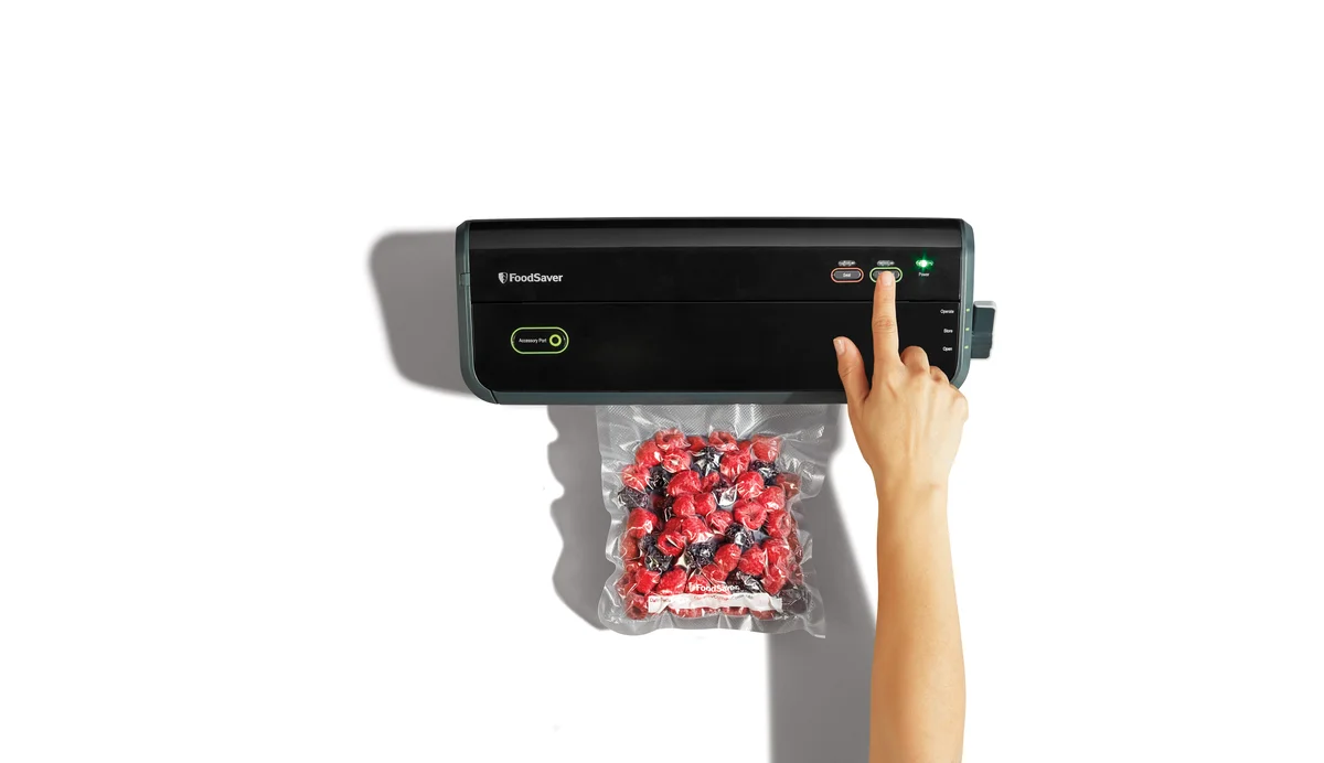 FoodSaver FM2000 in use with hand pressing vacuum seal button on a bag of strawberries