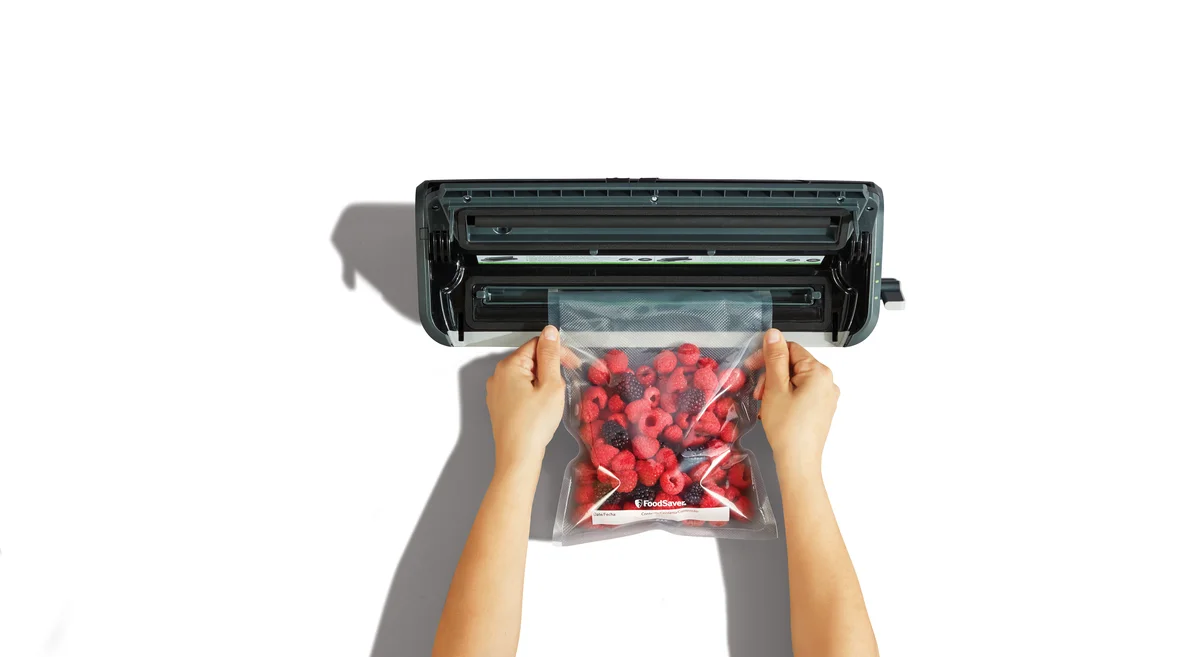 FoodSaver FM2000 top-down view with hands loading a vacuum seal bag of berries