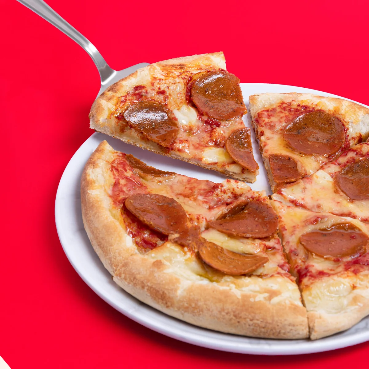 Blackbird Foods Pepperoni Pizza with a slice being lifted on a serving spatula, showing melted cheese and plant-based pepperoni