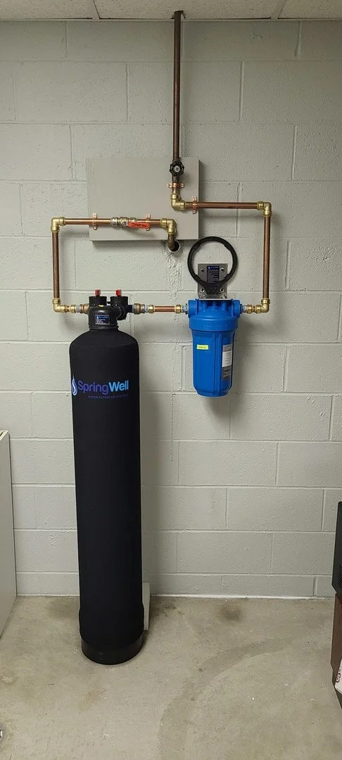 SpringWell CF1 carbon filter tank and blue sediment housing mounted with copper pipe plumbing in a basement