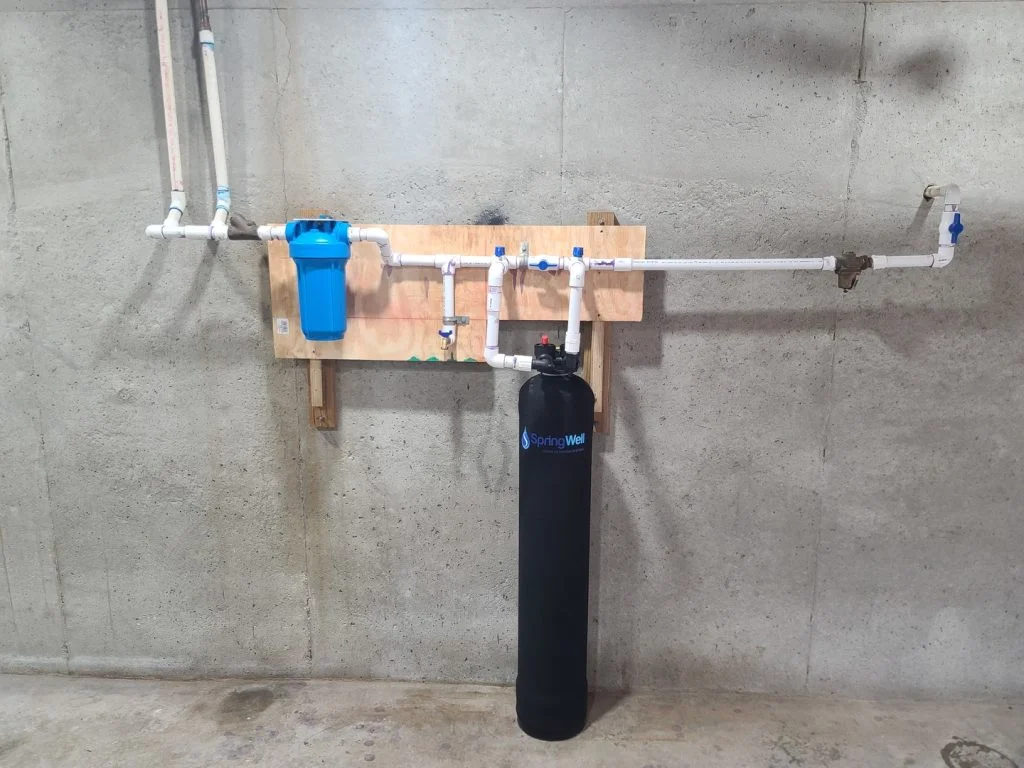 SpringWell CF1 whole house water filter system mounted on basement wall with full plumbing connections